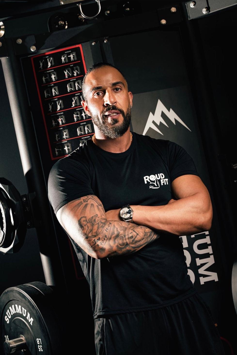 Coach Rudi Assaf, arms crossed, in a Roudfit tee at the gym